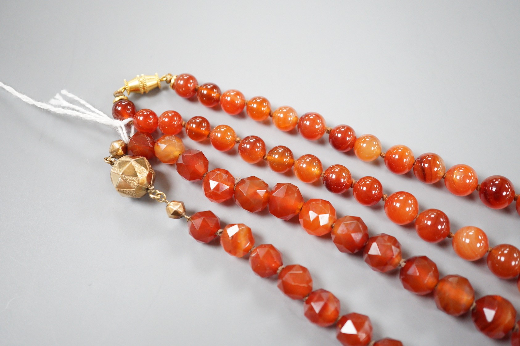 Two single strand carnelian necklace, one with facet cut beads, 44cm & 60cm, both with yellow metal clasps.